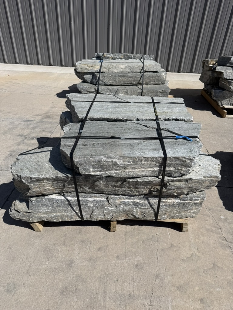 Pallets of gray natural stone stair treads and landscape benches at Rivers Edge Landscape Supply