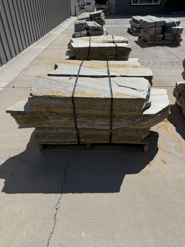 Pallets of tan natural stone stair treads and landscape benches at Rivers Edge Landscape Supply